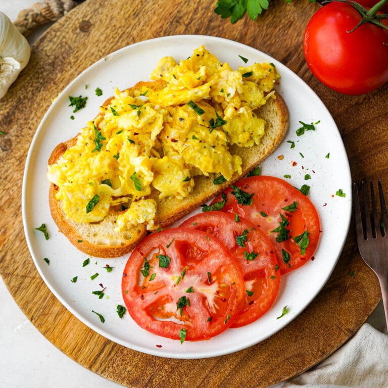 scrambled duck eggs on toast with sliced tomatoes on a white plate