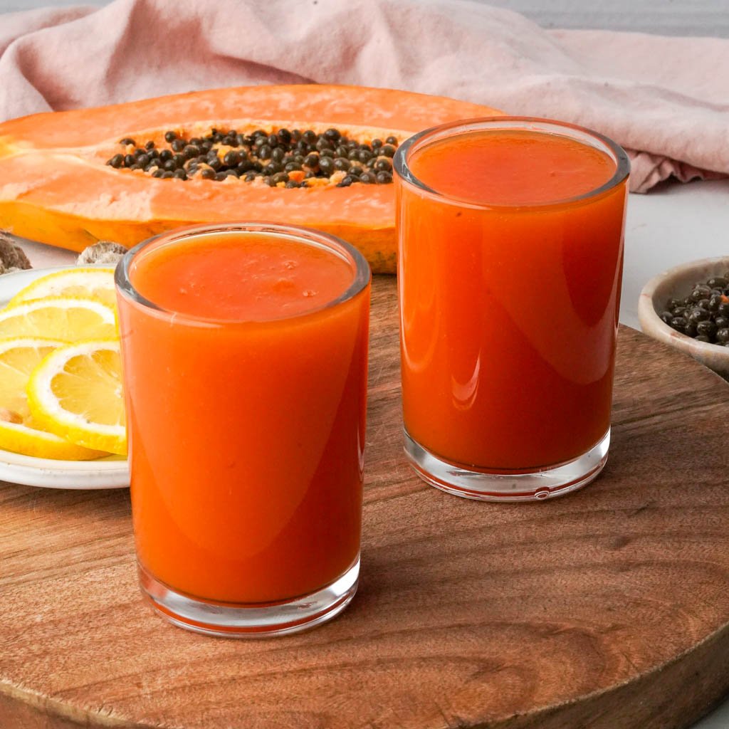 two cups of papaya juice with the ingredients in the background