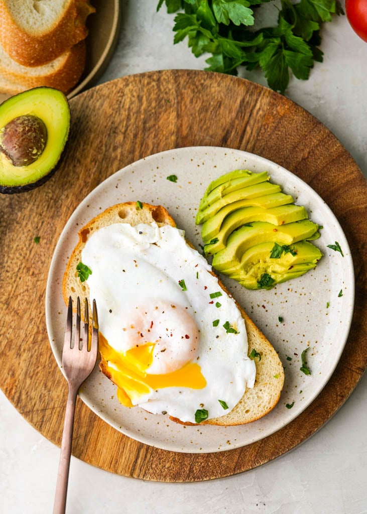 over easy duck egg on toast with avocado on the side on a white plate