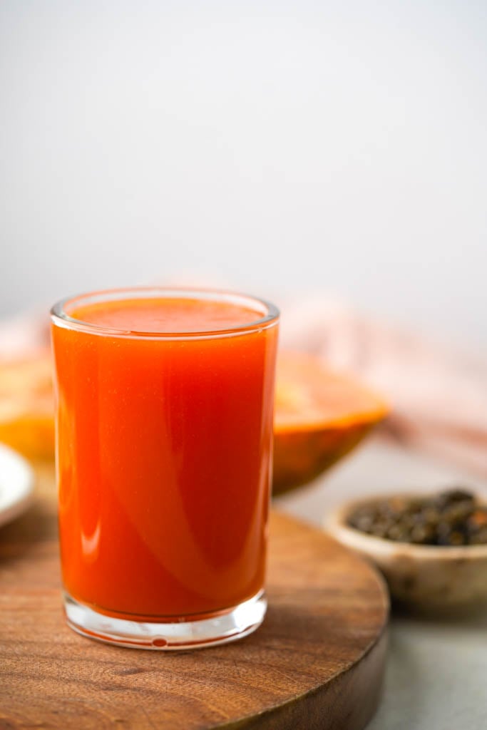 a glass of papaya juice with the ingredients in the background