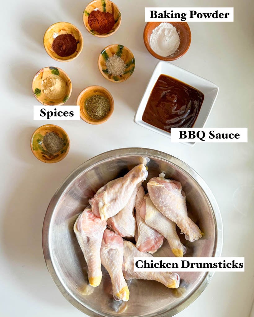 ingredients to make lollipop drumsticks shown is a large bowl of raw chicken drumsticks a small bowl of barbecue sauce small ramekins filled with various spices and a small ramekin of baking powder