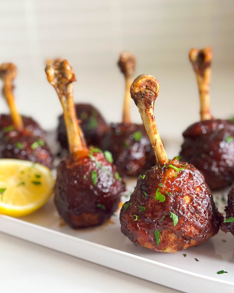 barbecue chicken lollipop drumsticks on a plate with a wedge of lemon