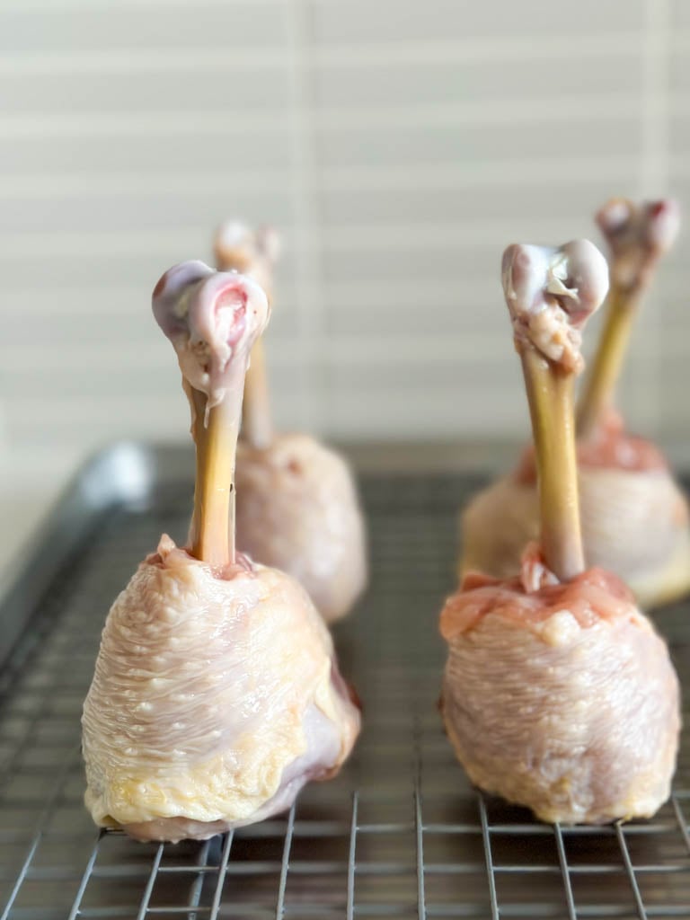 raw frenched chicken drumsticks on a wire rack lined baking dish