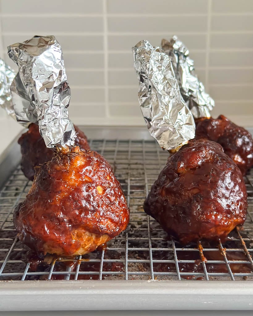 four chicken lollipop drumsticks fully cooked on a wire rack lined baking dish