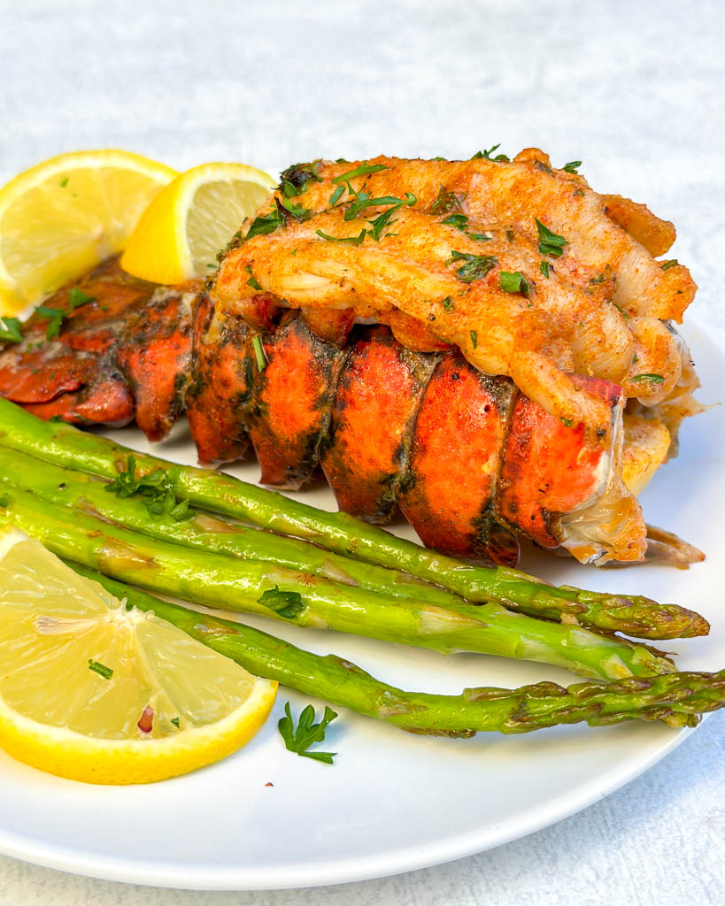 plated broiled lobster tails with asparagus and lemon wedges