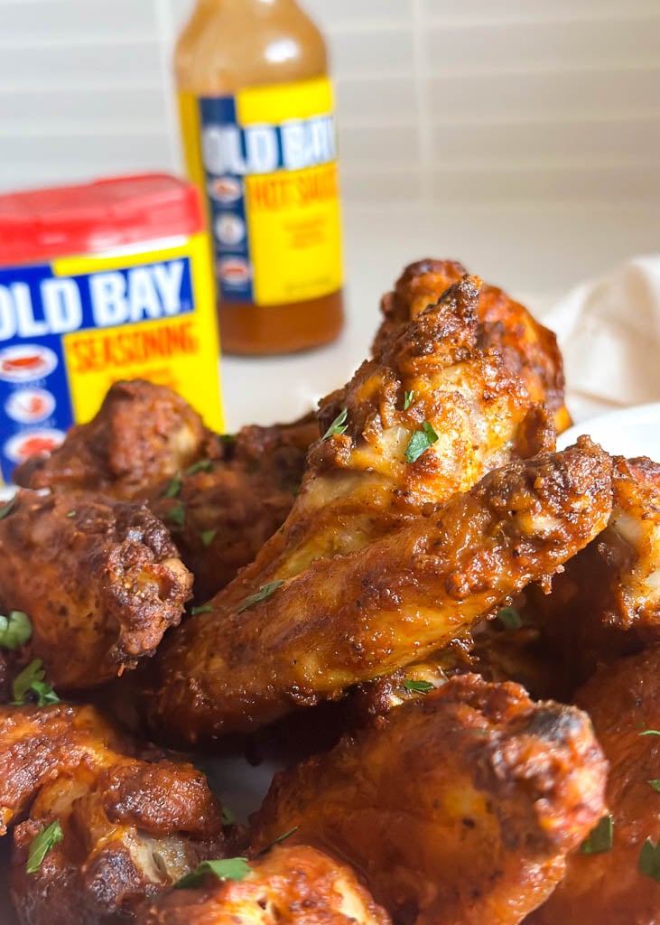 close up view of buffalo old bay wings with old bay seasoning and hot sauce in the background