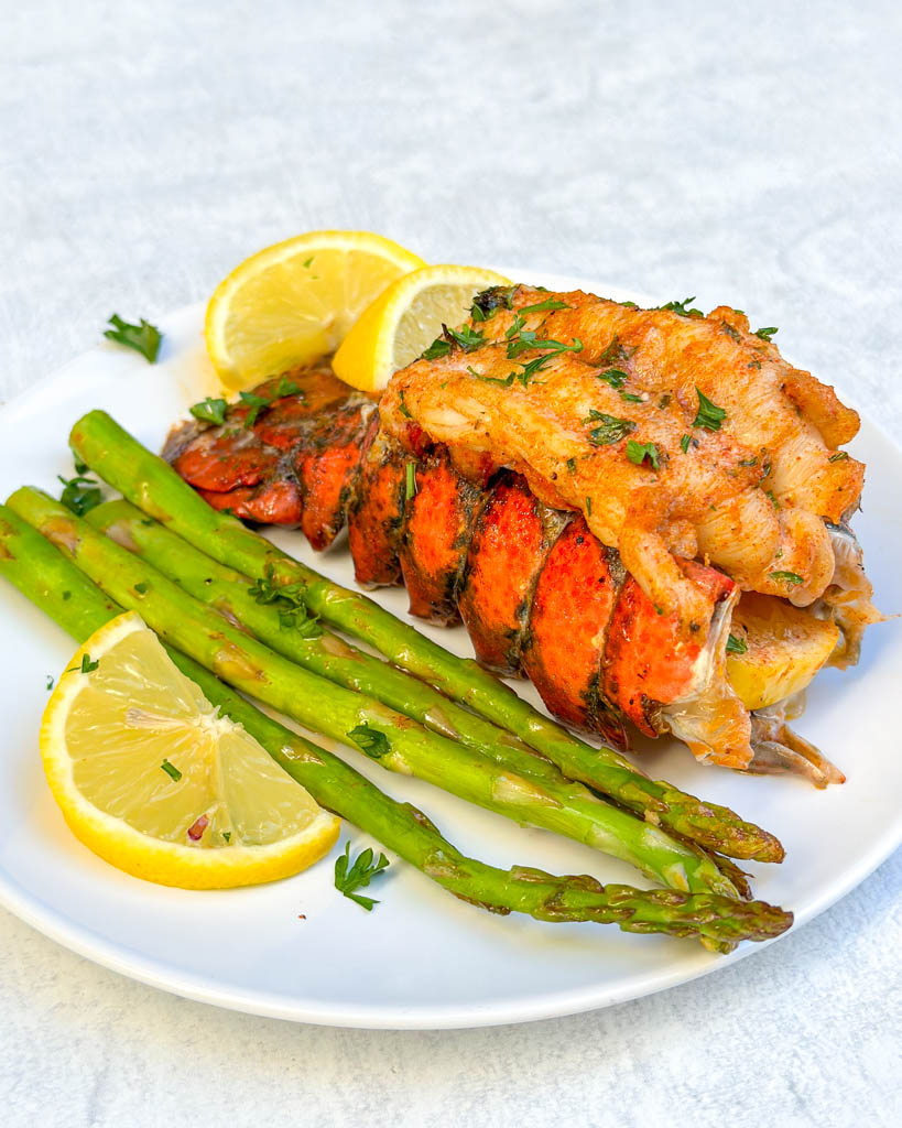 plated broiled lobster tails with asparagus and lemon wedges
