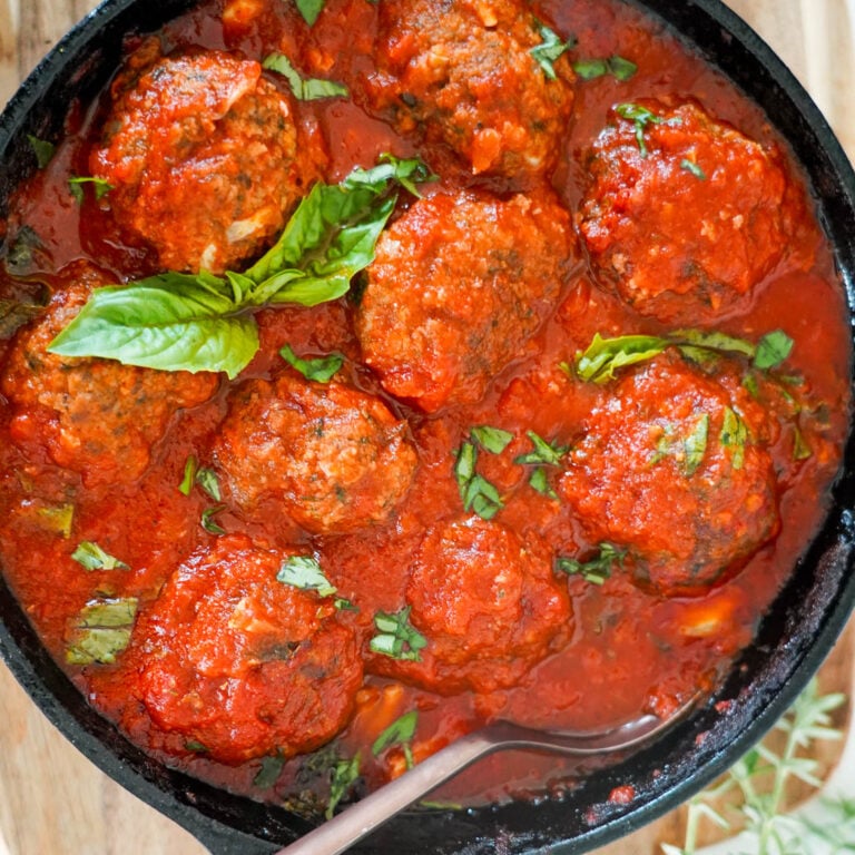 cast iron filled with gluten free meatballs covered in marinara sauce with a spoon in the dish and basil to garnish