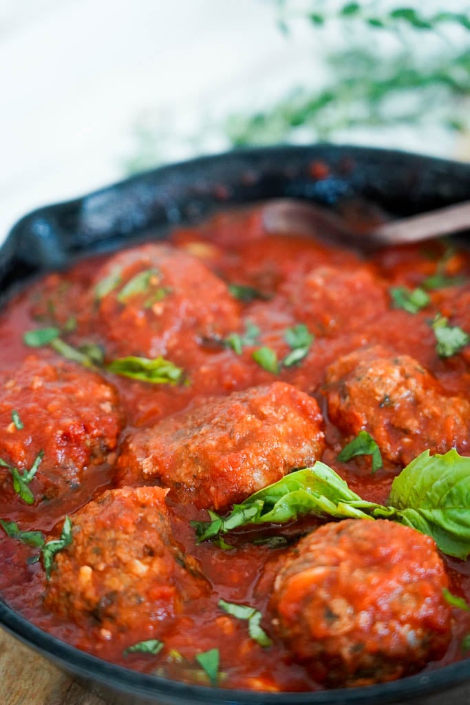 cast iron filled with gluten free meatballs covered in marinara sauce and basil to garnish