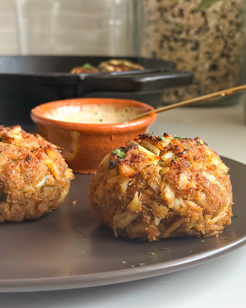 plated Maryland crab cakes with dipping sauce and a skillet in the background