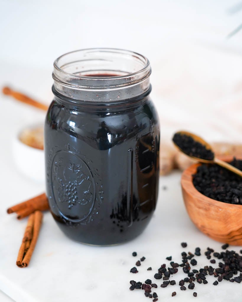 a jar of elderberry syrup surrounded by scattered cinnamon sticks and dried elderberries