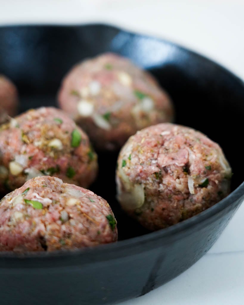 four gluten free meatballs in a cast iron dish before cooking