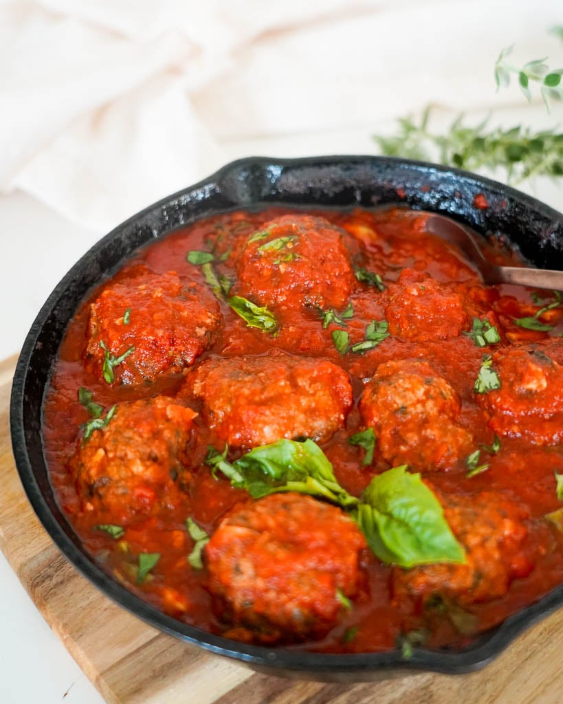 cast iron filled with gluten free meatballs covered in marinara sauce and basil to garnish