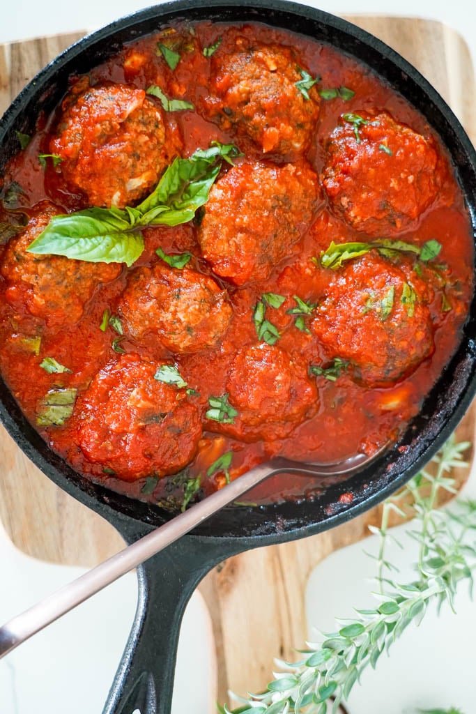 cast iron filled with gluten free meatballs covered in marinara sauce with a spoon in the dish and basil to garnish