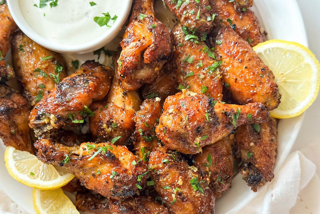 plated honey lemon pepper wings with a side of ranch dip and lemon wedges for garnish