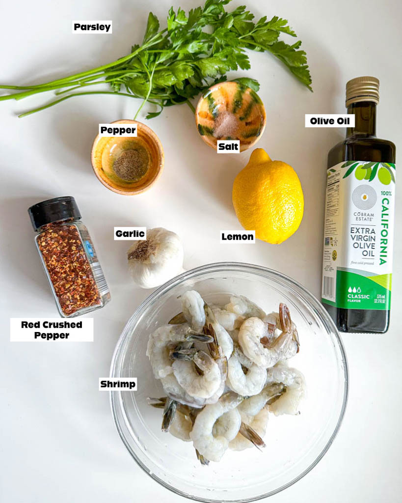 ingredients to make gambas al ajillo shown is a bowl of shrimp a bottle of olive oil a lemon a small ramekin of salt a small ramekin of pepper a bulb of garlic and parsley