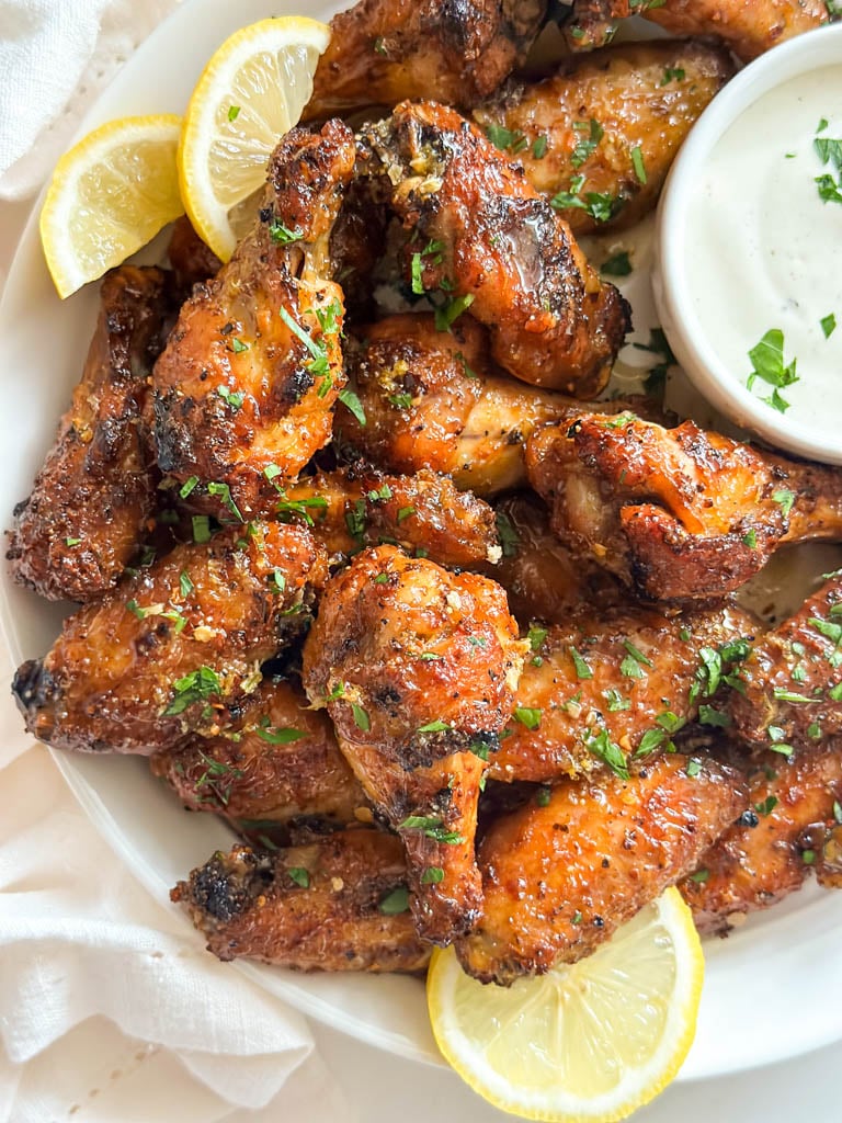 plated honey lemon pepper wings with a side of ranch dip and lemon wedges for garnish