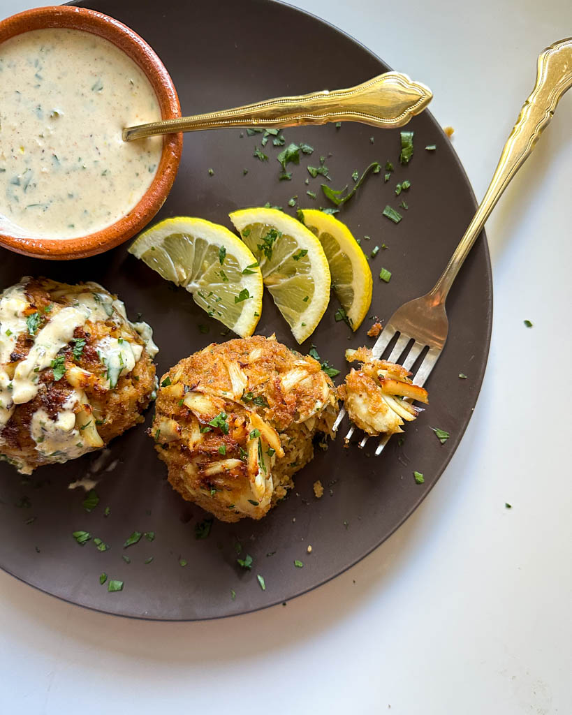 plated crab cakes with aioli drizzled over one and another with a fork beside it