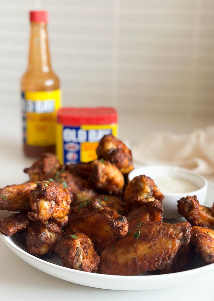 plated old bay chicken wings with old bay seasoning and hot sauce in the background