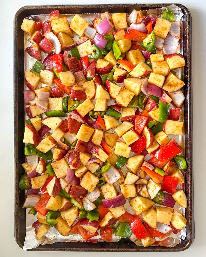 raw home fries and peppers on a foil lined baking sheet