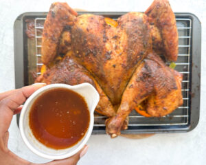 a small pouring cup with turkey drippings held overtop of a half way done turkey on a baking sheet tray
