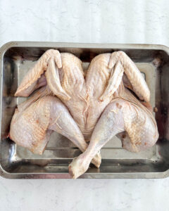 raw spatchcocked turkey placed flat in a roasting tray