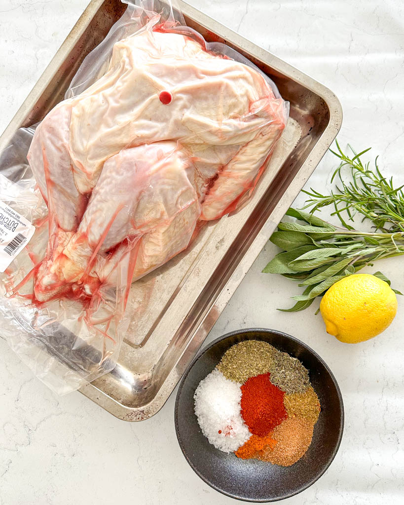 sealed turkey placed in a roasting tray a bowl of dry brine seasoning on the side a lemon and fresh herbs