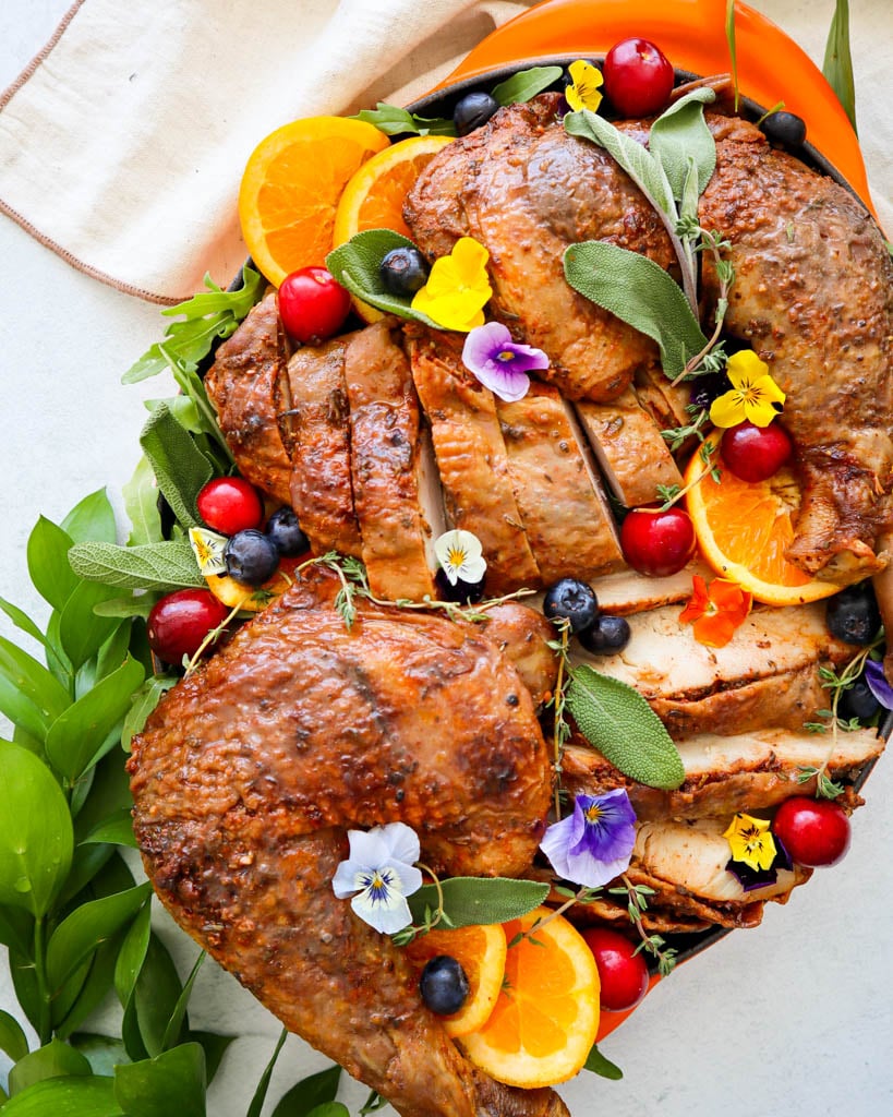 carved thanksgiving maple glazed turkey on a tray garnished with oranges edible flowers fresh herbs and cranberries