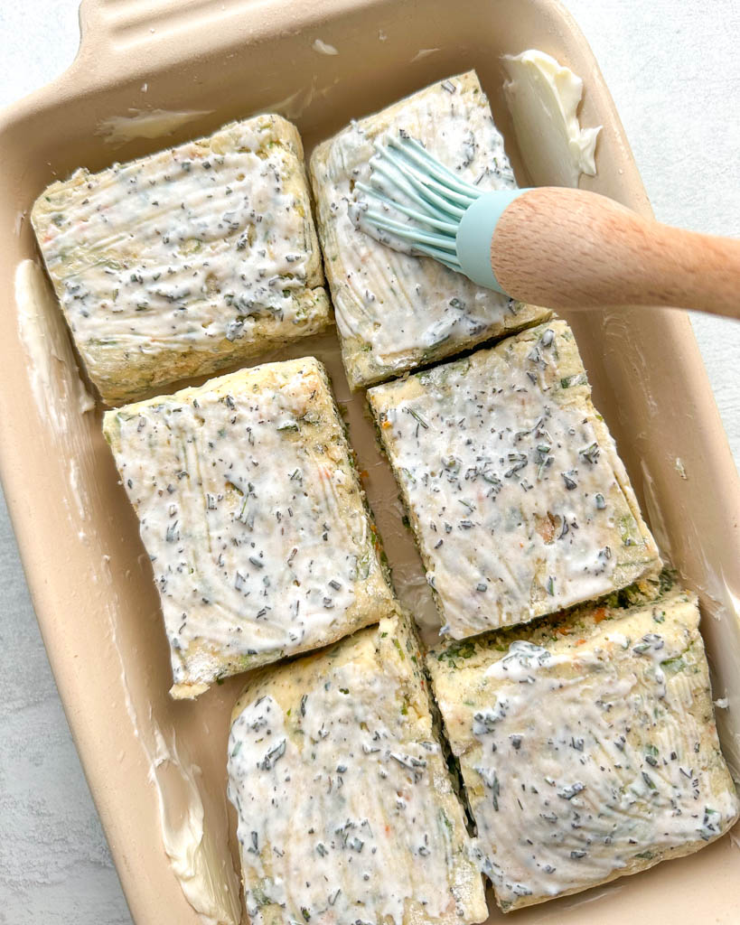 unbaked gluten-free biscuits being slathered with herbs and buttermilk