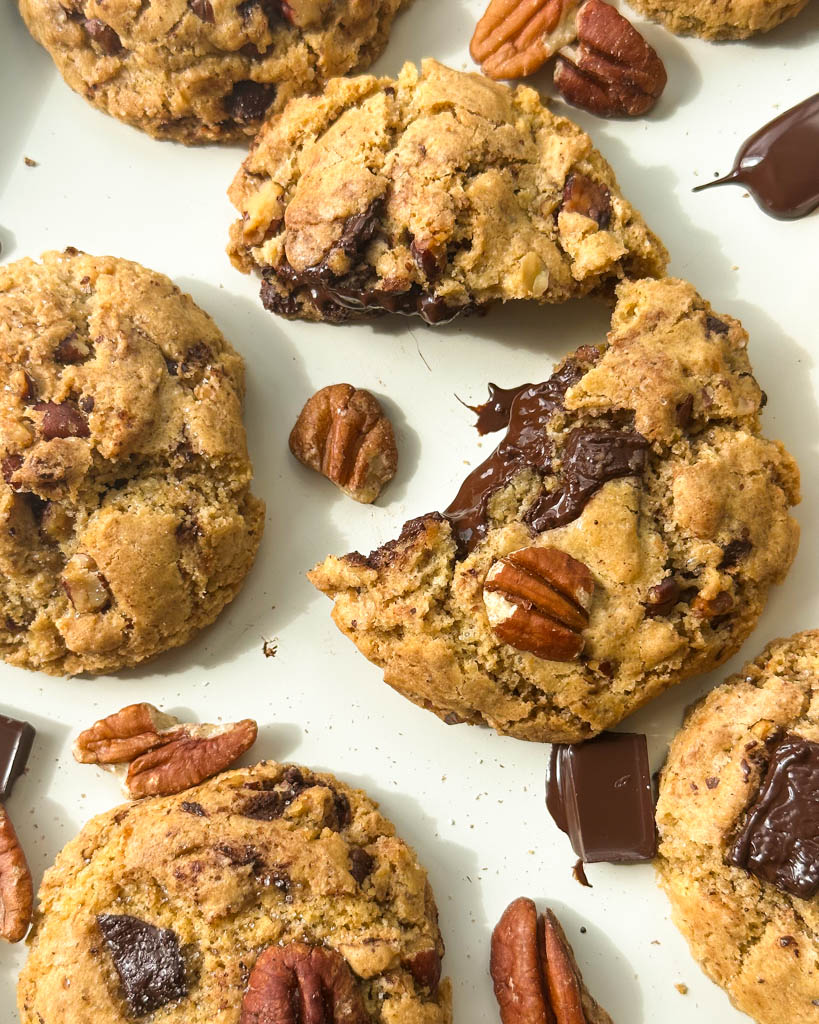 scattered butter pecan chocolate chip cookies with one cut open to reveal gooey center