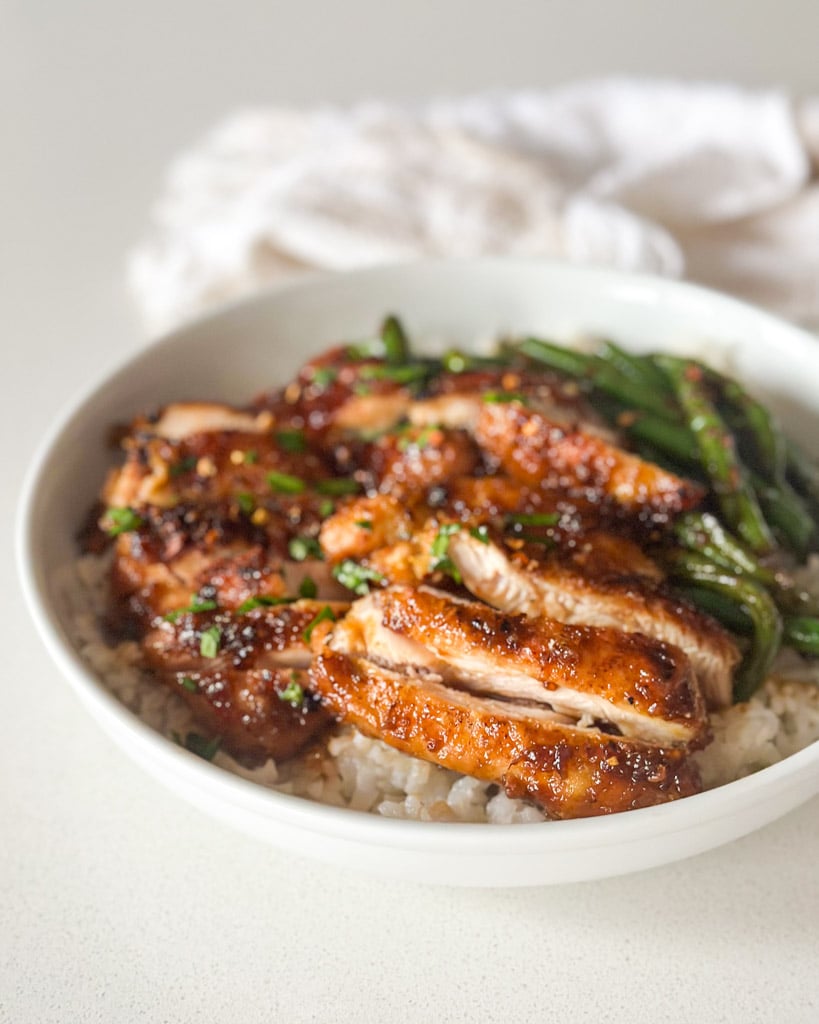 a bowl of rice with sliced honey ginger chicken thighs on top with a side of green beans