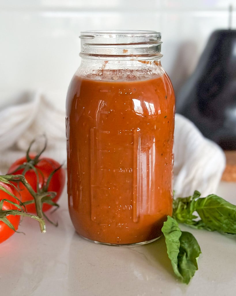 a mason jar filled with homemade marinara sauce two tomatoes and basil leaves are next to the jar