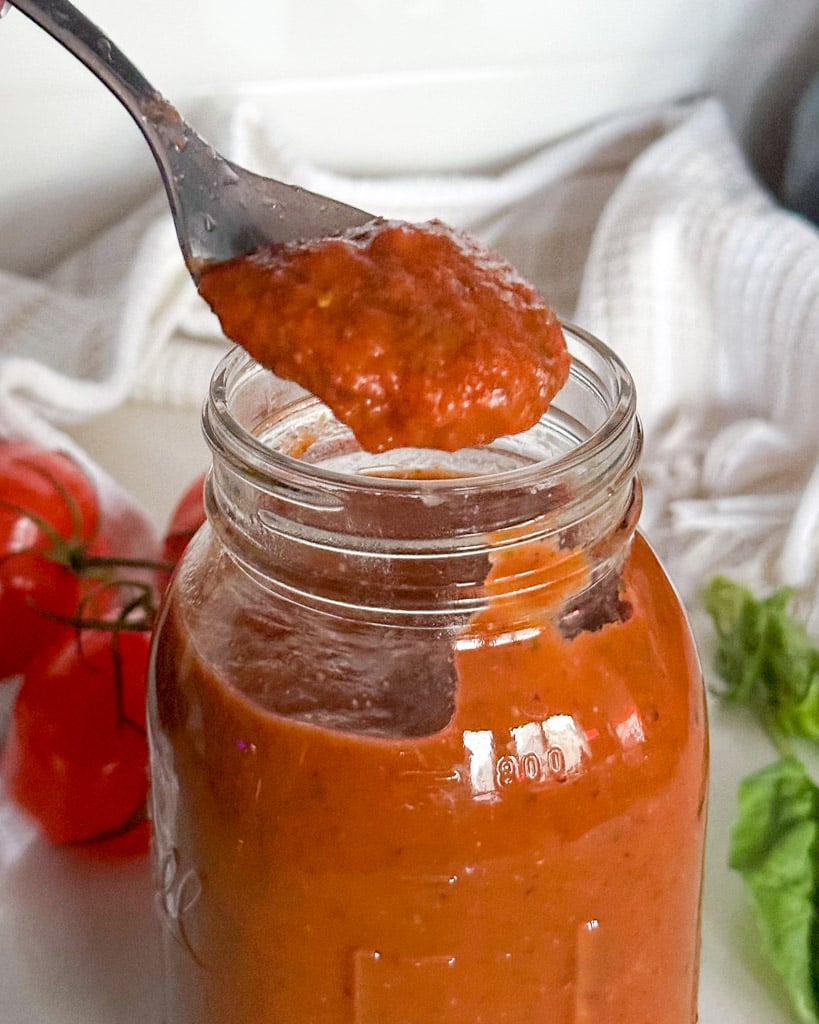 marinara sauce in a jar with a spoon holding sauce on top