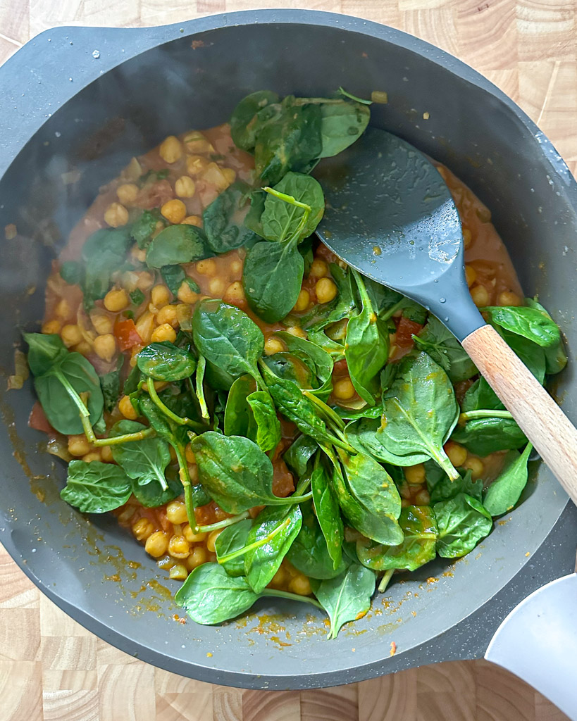 spinach added to chickpea curry in a large skillet