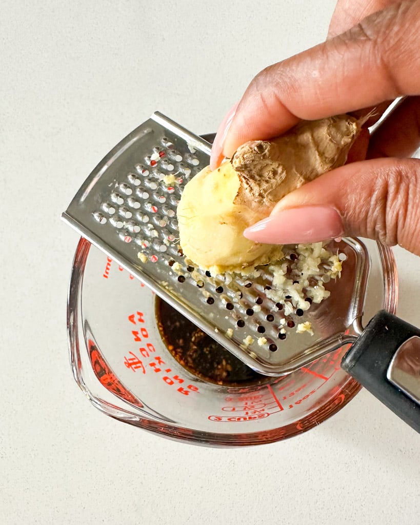 grating ginger on a microplane placed over a cup of soy sauce