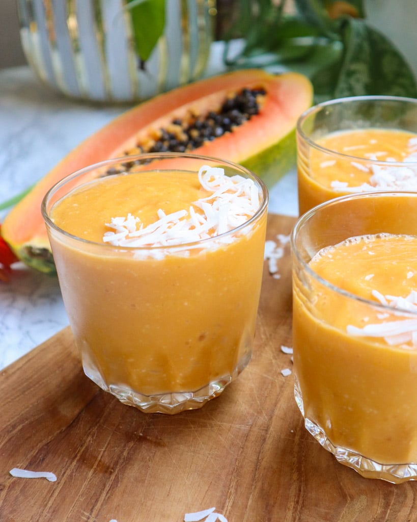 three glasses of papaya smoothie with a half of papaya sliced in the background