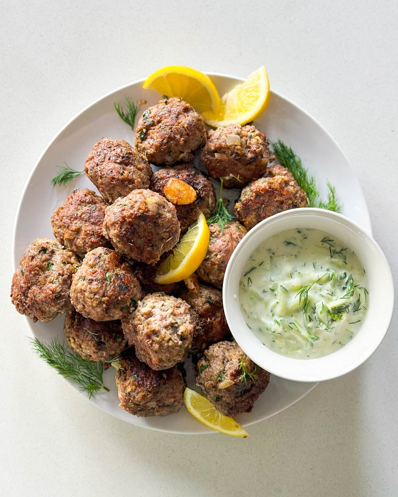lamb meatballs on a plate with sliced lemon and a small bowl of tzatziki sauce