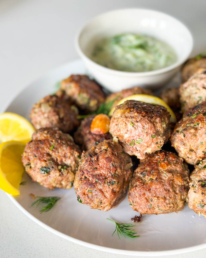 lamb meatballs on a plate with sliced lemon and a small bowl of tzatziki sauce