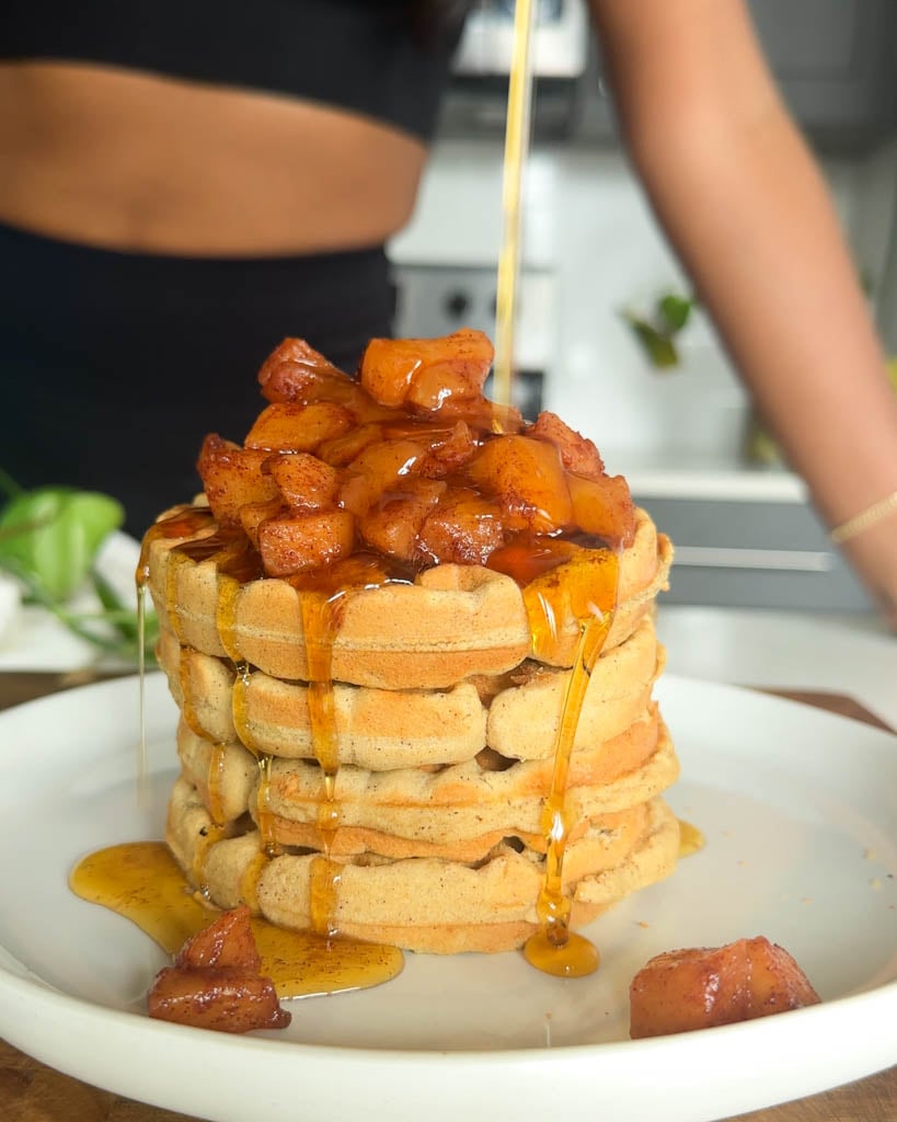 a stack of gluten free grain free high protein almond flour waffles with stewed apples on top and syrup pour onto waffles