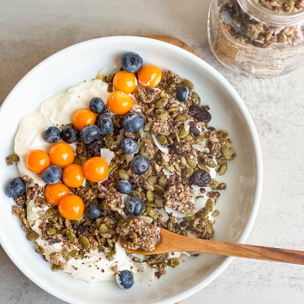 bowl of grain free super seed granola and yogurt with berries and a small wooden spoon