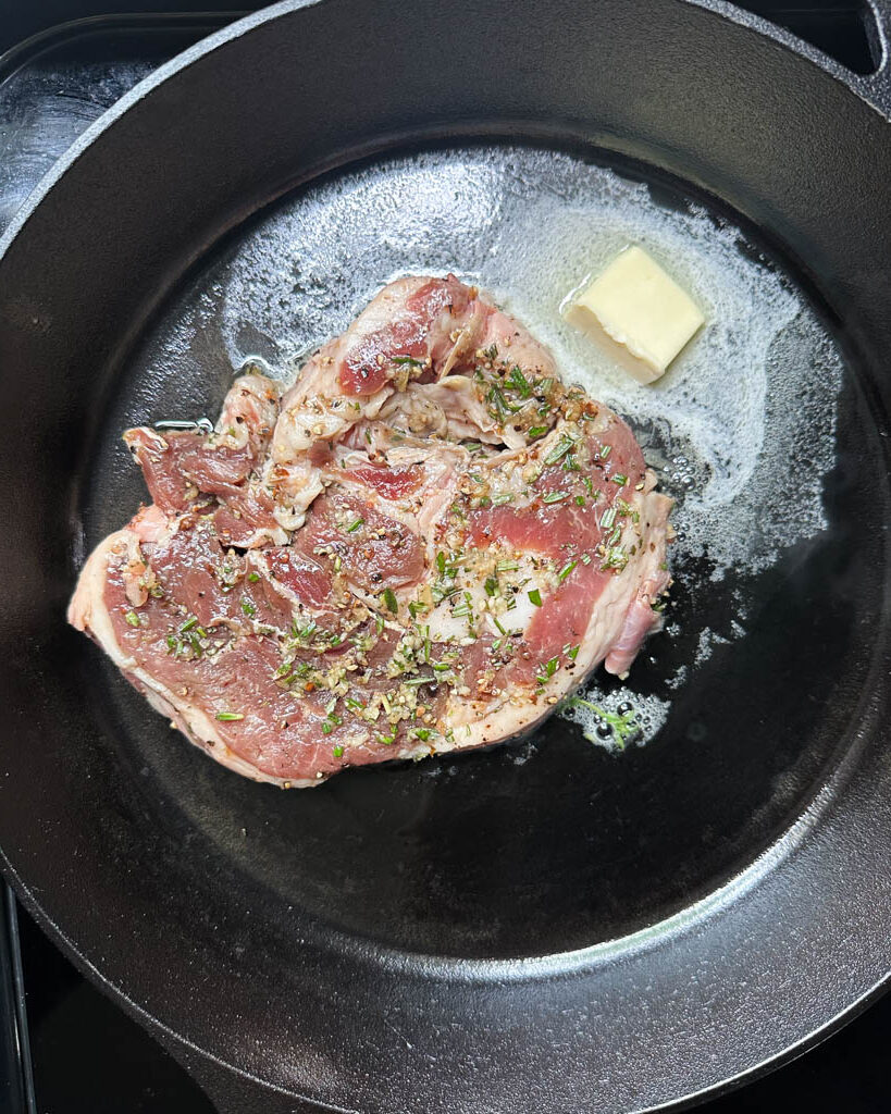 raw lamb steak in a cast iron with butter