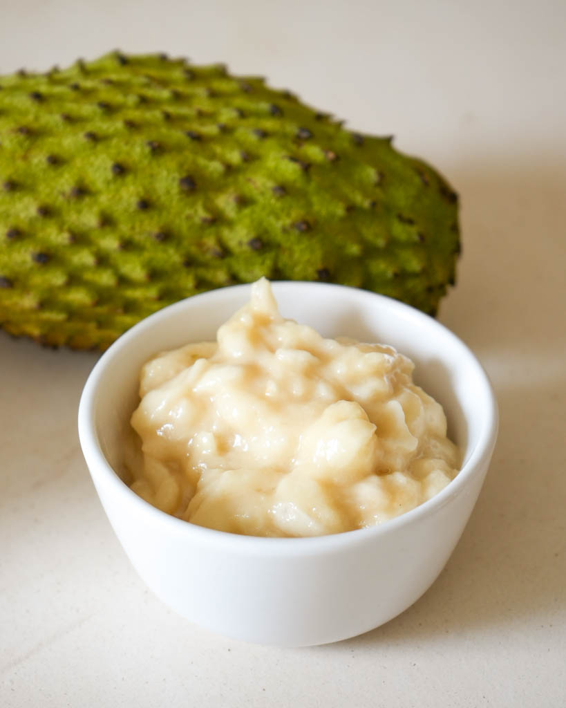 fresh guanabana pulp in a small white bowl with a whole guanabana behind the bowl