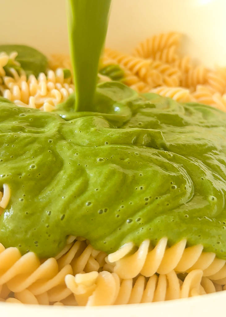 green zucchini pasta sauce being poured on gluten free rigatoni noodles