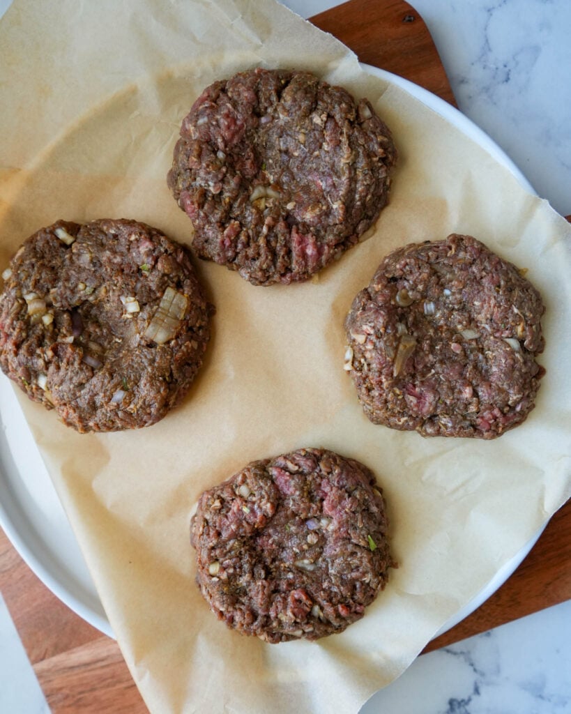 four raw ground bison patties on a parchment lined plate