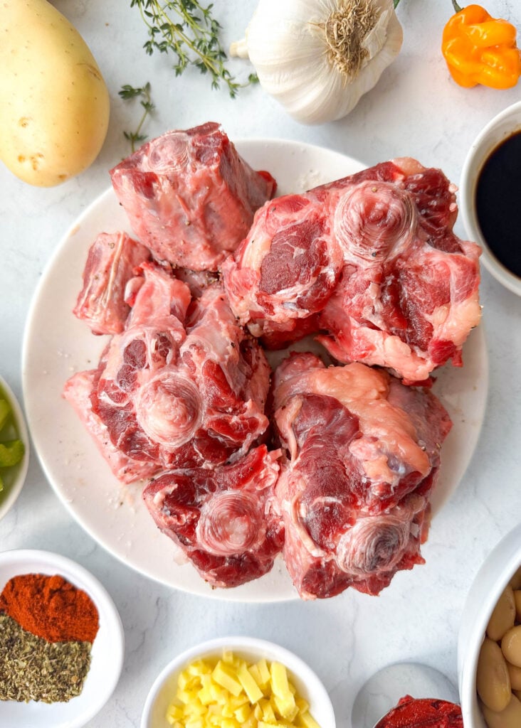 raw oxtail on a plate surrounded by ingredients to make oxtail stew