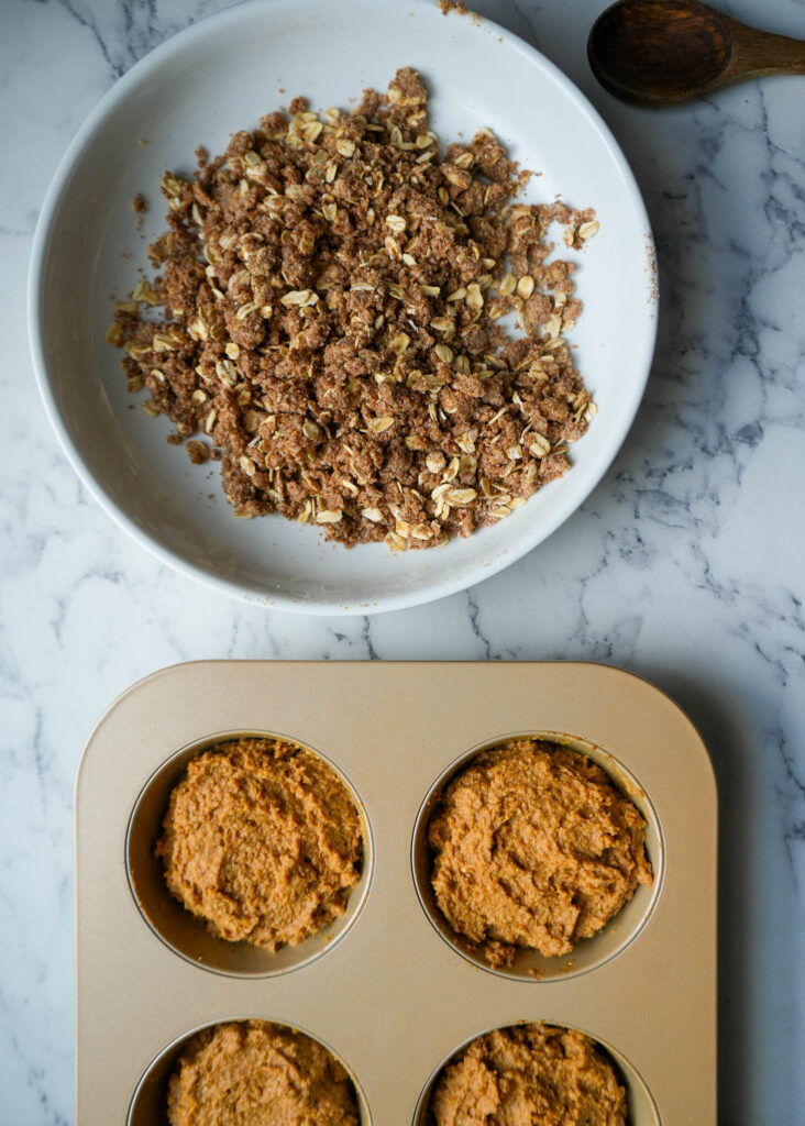 pumpkin batter in a muffin tin and streusel topping in a large bowl