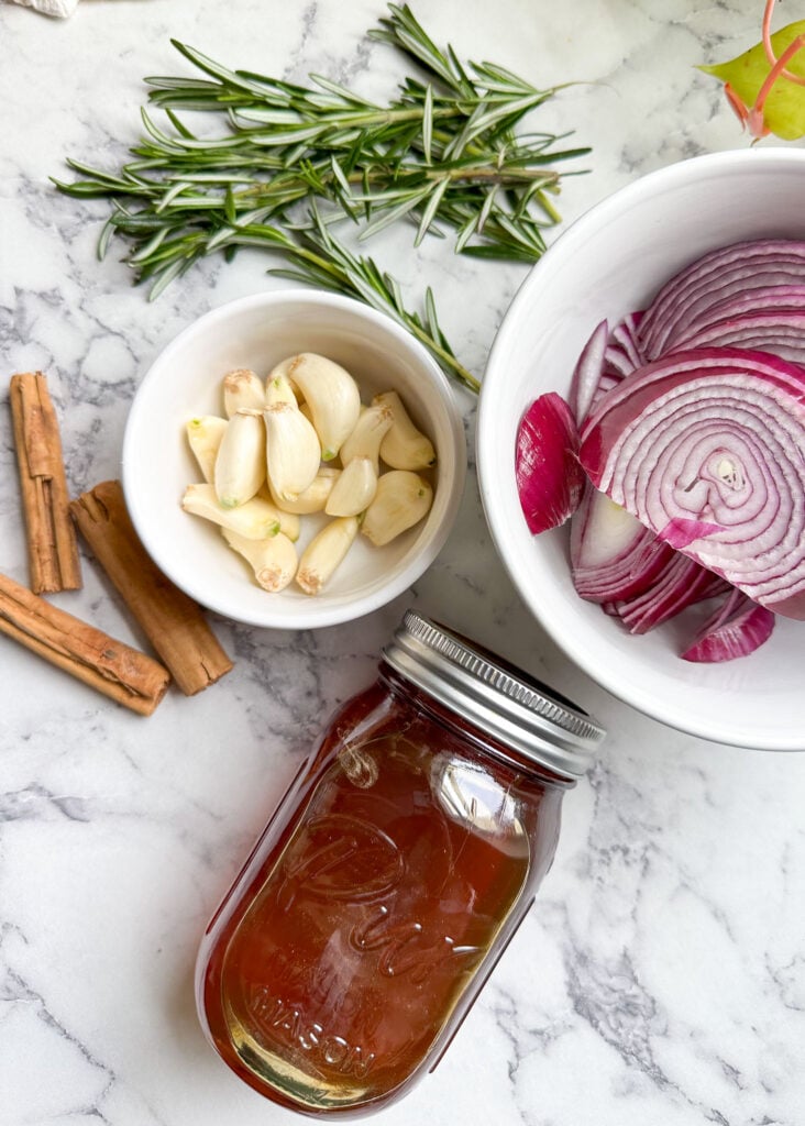 ingredients to make honey cough syrup shown are cinnamon sticks garlic cloves onion a jar of raw honey and rosemary stalks