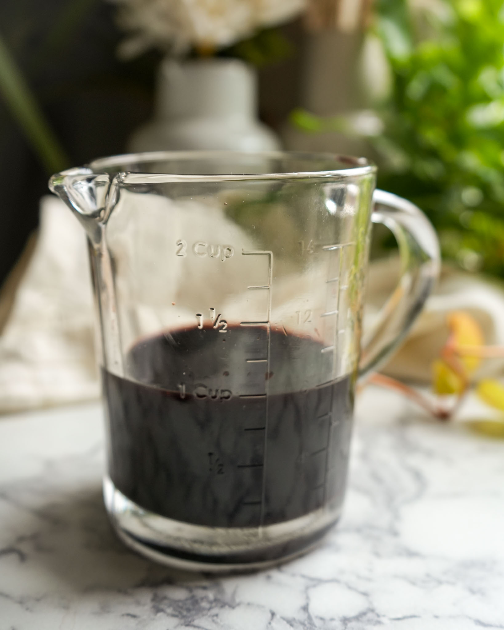 A measuring cup filled with dark, rich elderberry syrup, ready for gummy preparation.