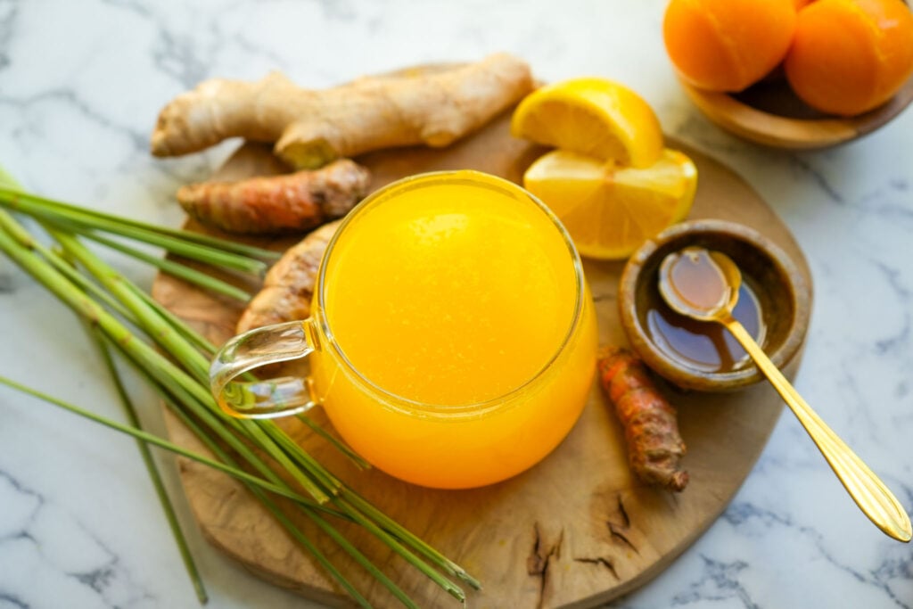 A glass mug of bright yellow lemon turmeric tea surrounded by fresh ingredients on a rustic wooden background.