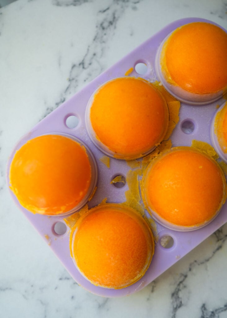 A silicone mold filled with frozen lemon turmeric bombs, showcasing their vibrant orange color.